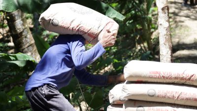 Salah satu sosok yang mencerminkan semangat tersebut adalah Santo, warga setempat yang setiap hari ikut bergotong royong mengangkut sak-sak semen menuju lokasi pengecoran. Dengan memikul beban puluhan kilogram di pundaknya