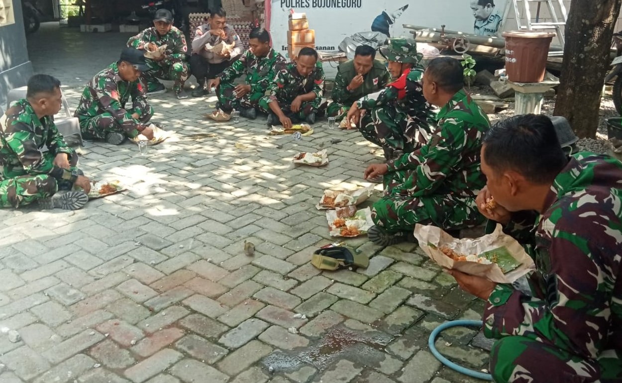 Usai mengerjakan berbagai sasaran fisik, personel Satgas TMMD ke-129 Kodim 0813/Bojonegoro beristirahat sejenak dengan menikmati makan siang menggunakan nasi bungkus sambil duduk lesehan di lokasi pekerjaan, Rabu (22/7/2026).