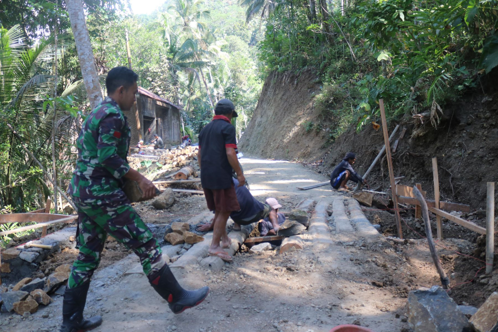 Di Dusun Kunir RT 01/RW 09, Desa Gumelem Kulon, Kecamatan Susukan, personel Satgas TMMD bersama masyarakat bahu-membahu mengangkut batu kali sebagai material pondasi pembangunan plat beton, Kamis (23/7/2026).