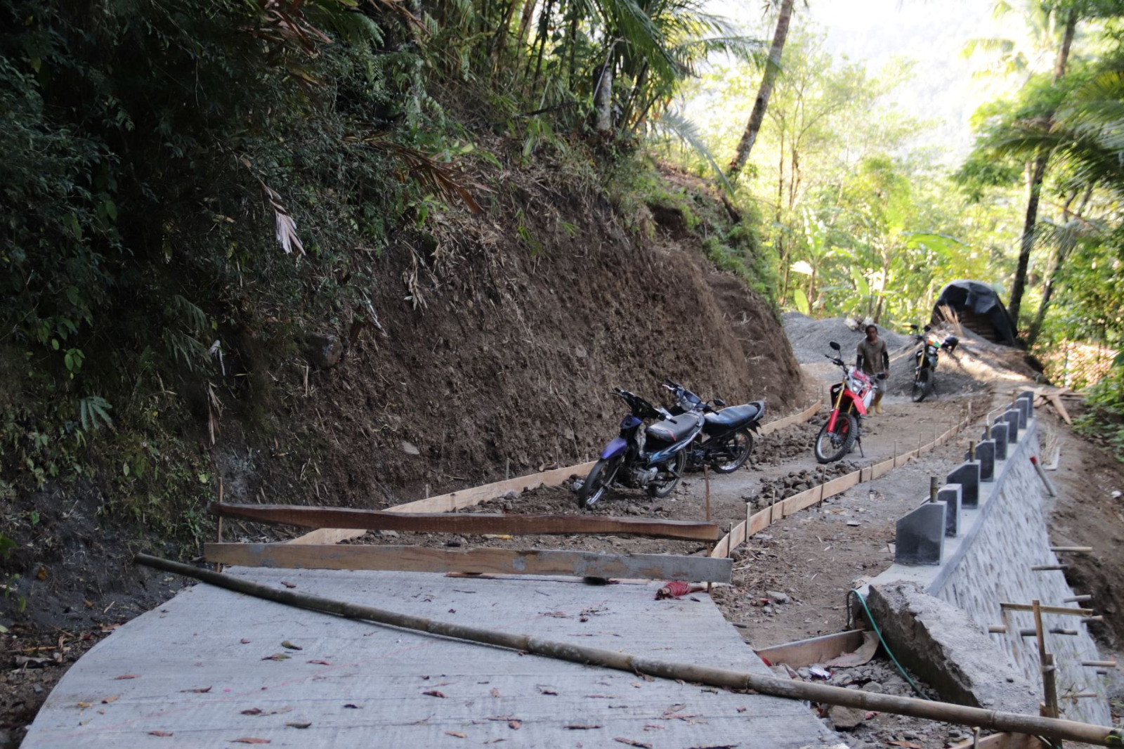 Personel Satgas TMMD dan warga bahu-membahu mengangkut pasir, batu, serta semen, sementara mesin molen terus berputar tanpa henti. Di sisi lain, sejumlah anggota Satgas meratakan adukan beton agar menghasilkan konstruksi jalan yang kuat, rapi, dan tahan lama.