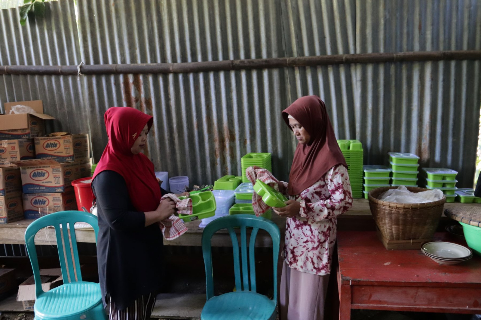 Bu Miswati tampak sibuk membersihkan serta menata kotak makan yang akan digunakan untuk mendistribusikan makanan kepada para pekerja di lokasi pembangunan, Selasa (28/7/2026).