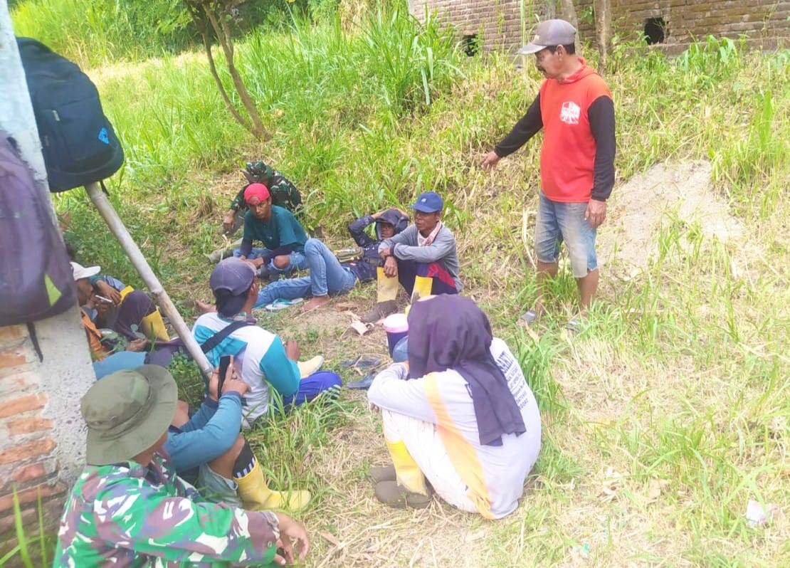 Suasana hangat tampak saat sejumlah prajurit TNI bersama warga memanfaatkan waktu istirahat dengan duduk lesehan di bawah rindangnya pepohonan di tepi jalan. Sambil menunggu kedatangan truk pengangkut material cor beton, mereka menikmati secangkir kopi dan berbincang santai tanpa sekat.