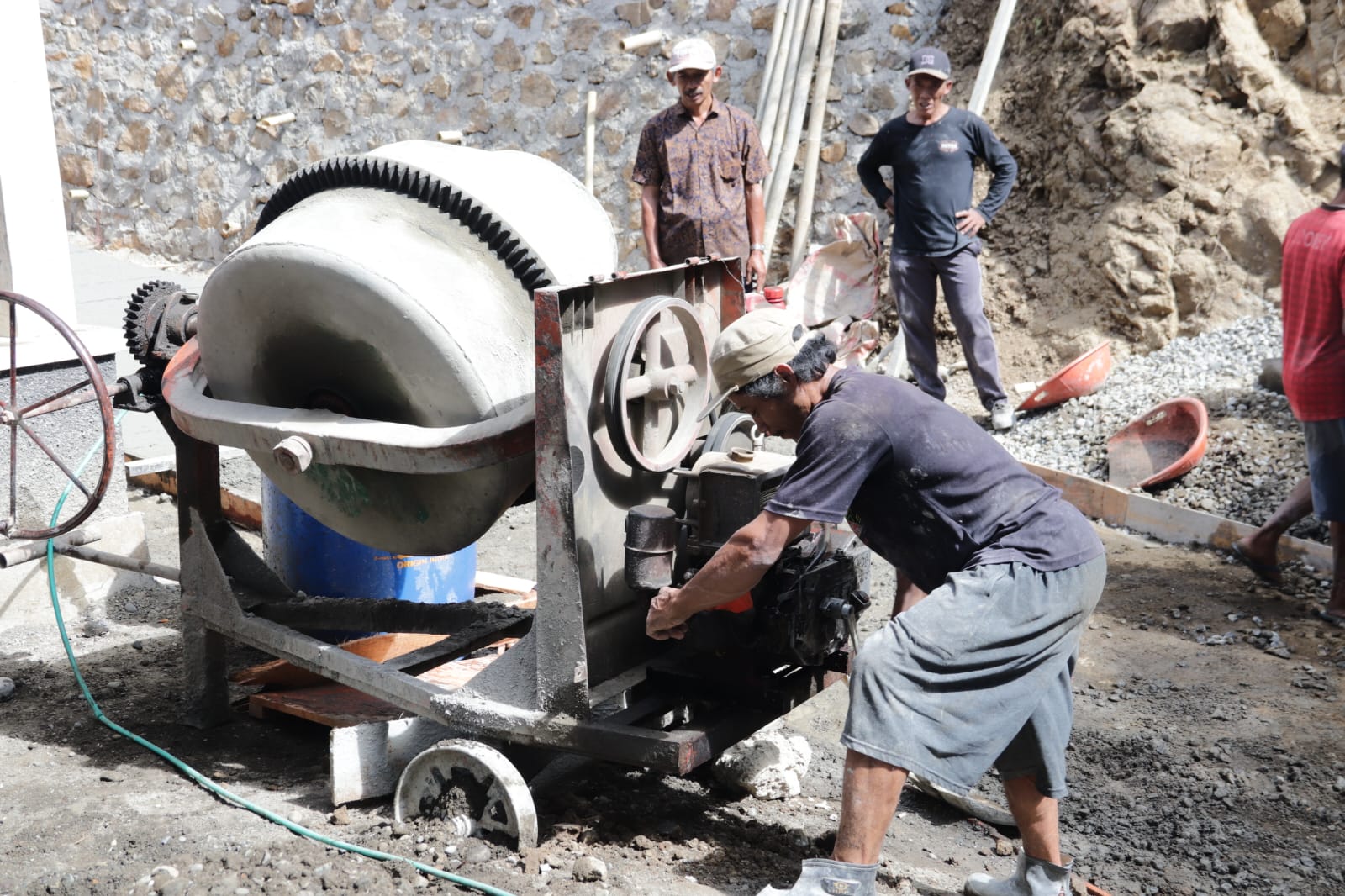 Madrohim, salah seorang warga, mengambil bagian dengan mengoperasikan mesin molen yang menjadi pusat pengolahan adukan beton, Minggu (26/7/2026).