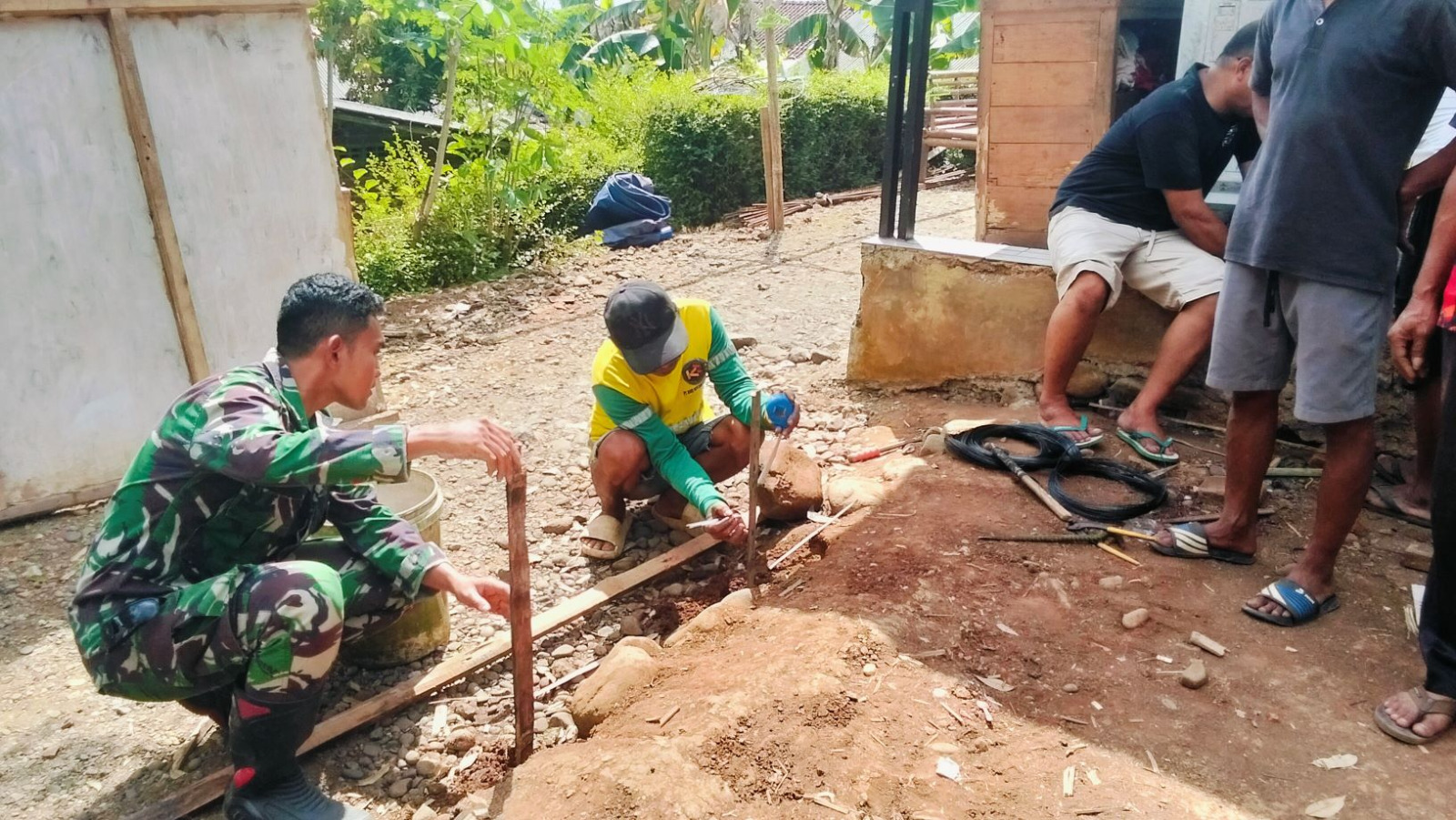 Salah satu tahapan penting yang dilakukan adalah pengukuran ketinggian pondasi menggunakan selang waterpass oleh Praka Agit bersama warga Bagio (51), Selasa (21/07/2026).