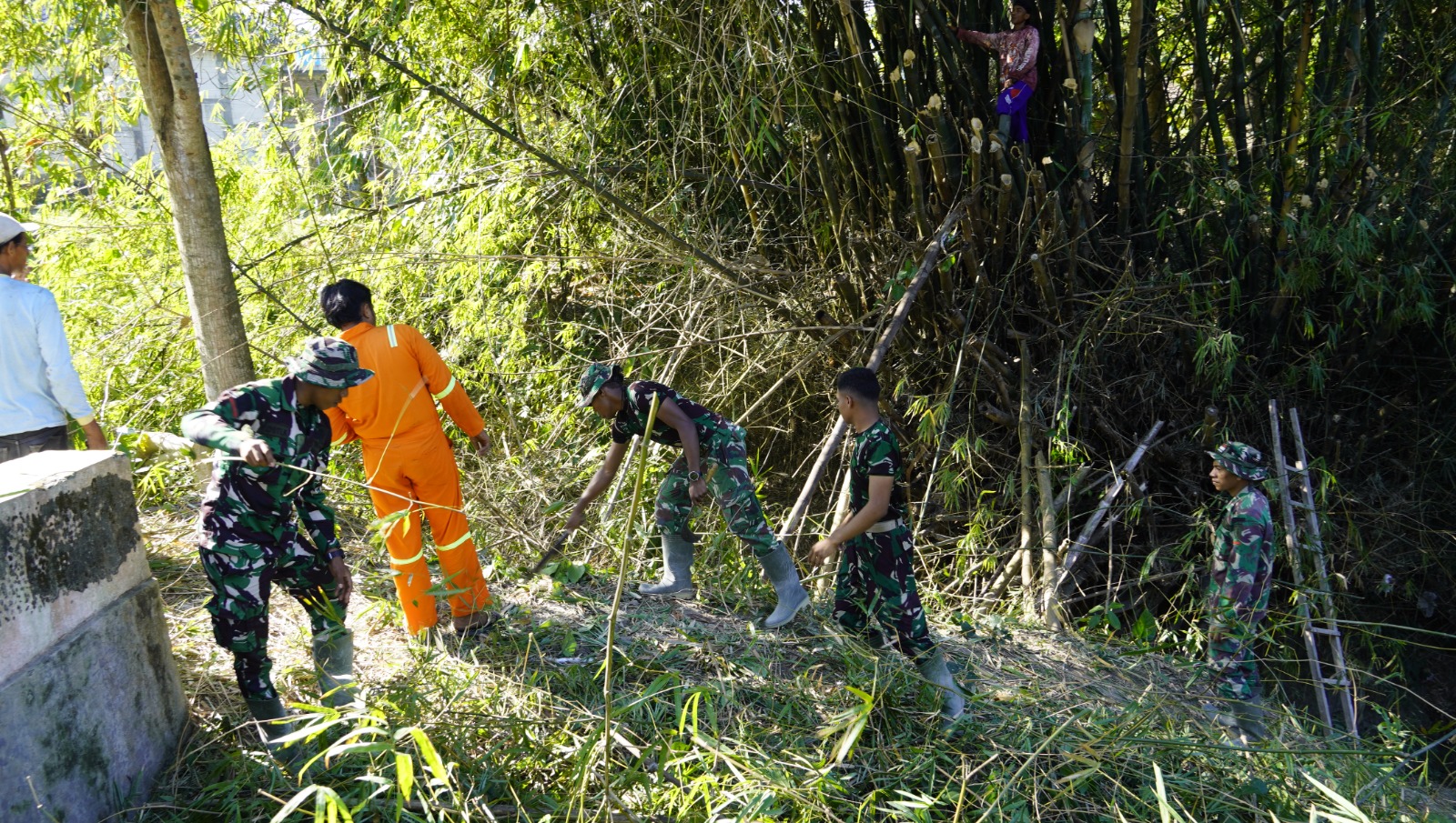 Melalui aksi gotong royong, personel Satgas TMMD bersama masyarakat melaksanakan kerja bakti membersihkan bantaran Sungai Kesongo di sekitar Jembatan Brang Etan, Desa Kesongo, Kecamatan Kedungadem, Minggu (26/7/2026).