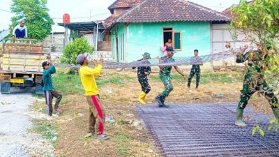 Personel Satgas TMMD bersama masyarakat bahu-membahu menurunkan material besi yang akan digunakan untuk pembangunan jalan cor beton di Dusun Kedungpandan, Rabu (22/7/2026).