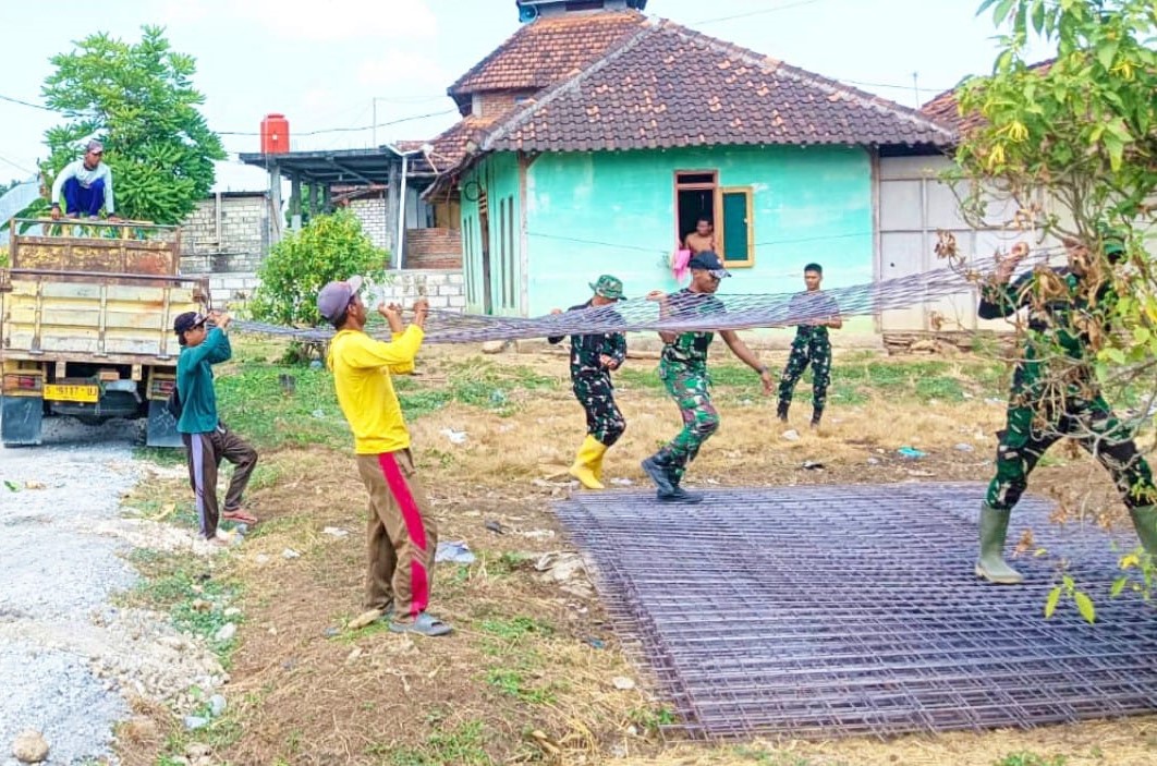 Personel Satgas TMMD bersama masyarakat bahu-membahu menurunkan material besi yang akan digunakan untuk pembangunan jalan cor beton di Dusun Kedungpandan, Rabu (22/7/2026).