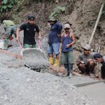 Salah satunya diperlihatkan Pratu Iwan yang tanpa henti mendorong angkong berisi adukan beton menuju titik pengecoran jalan, Jumat (31/7/2026).