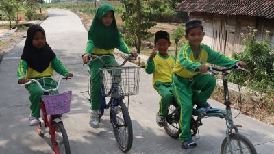 Dengan sepeda yang mereka kayuh penuh semangat, perjalanan menuju sekolah kini terasa lebih nyaman setelah akses jalan di wilayah mereka berubah menjadi lebih baik.