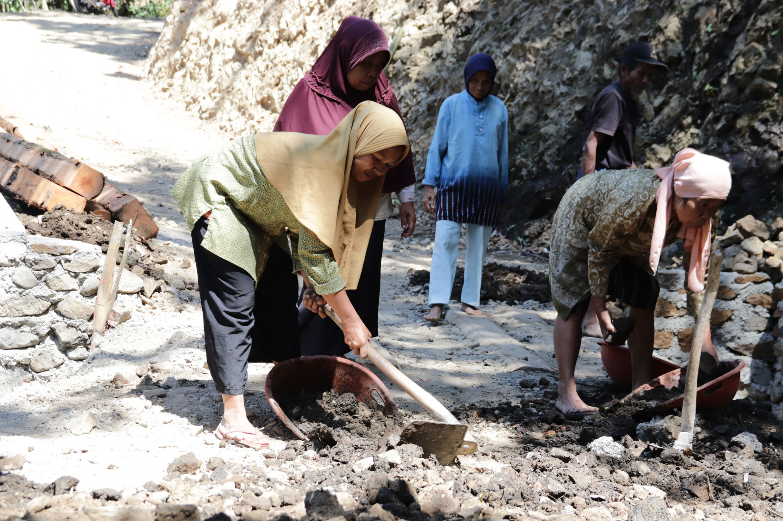 Dengan penuh semangat, ia mendorong angkong berisi tanah untuk mendukung pekerjaan pengecoran rabat beton sepanjang 737 meter, lebar 2,5 meter, dan tebal 0,15 meter di Dusun Kunir RT 01/09, Desa Gumelem Kulon, Kecamatan Susukan, Senin (27/07/2026).