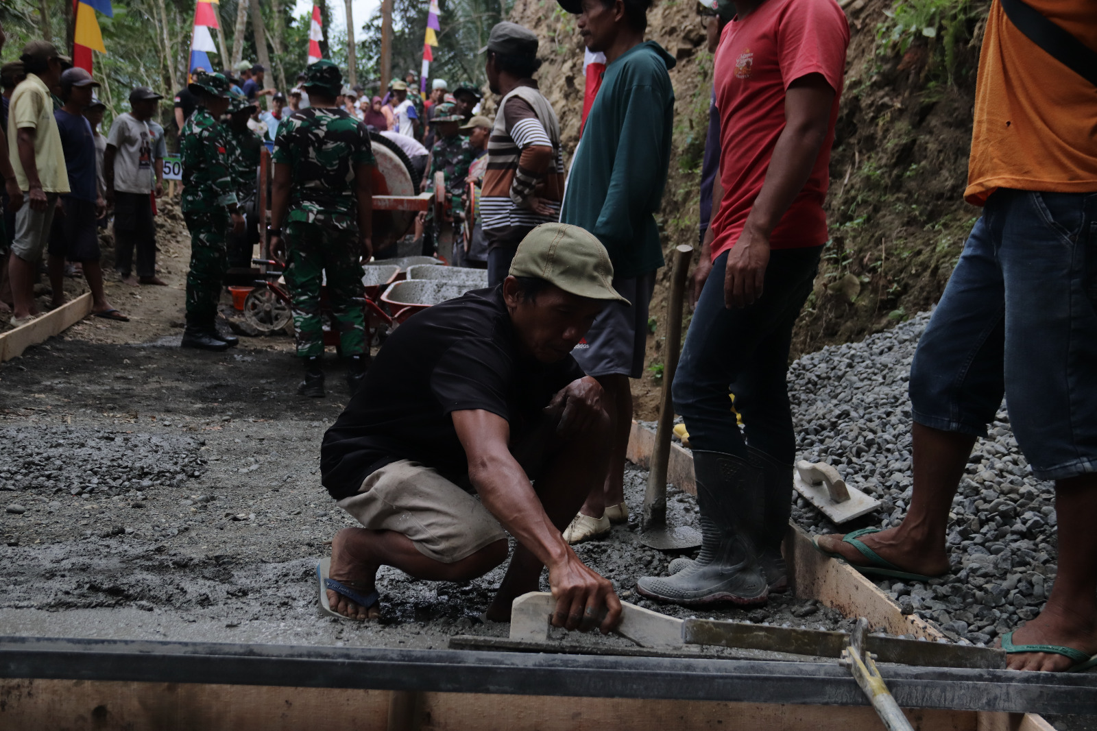 Desa Gumelem Kulon, Kecamatan Susukan, Kabupaten Banjarnegara. Di tengah proses pembangunan jalan rabat beton, seorang warga, Matrohim (50), tampak antusias bergabung bersama personel Satgas TMMD meratakan adukan beton, Kamis (16/7/2026).
