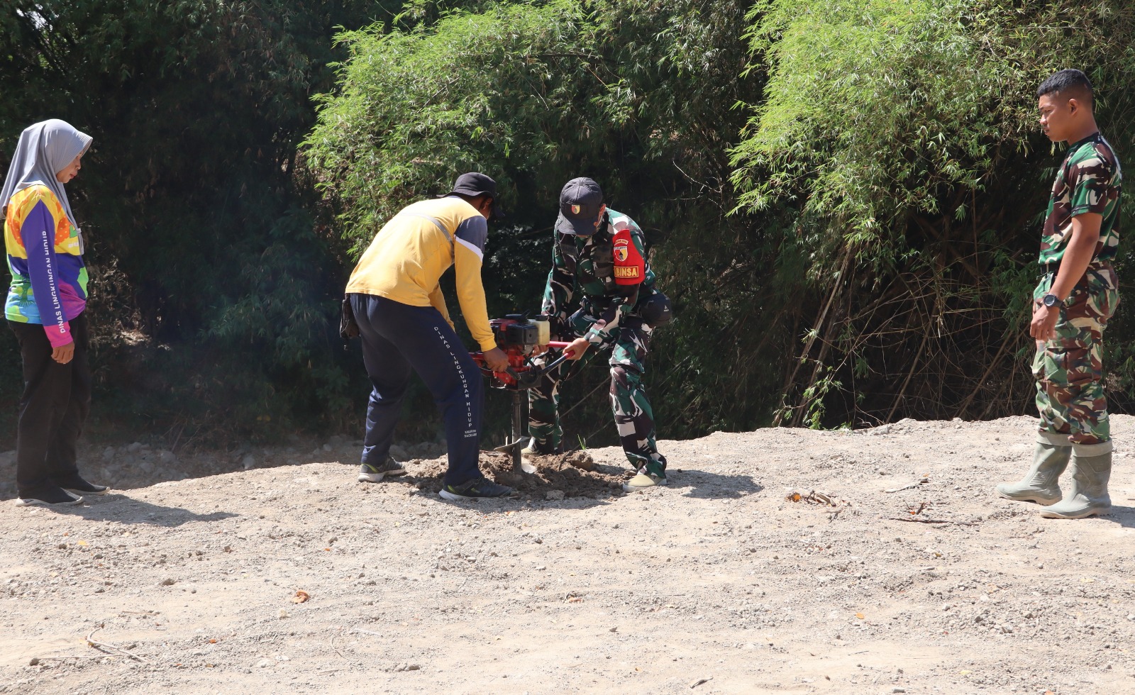 Babinsa Desa Kesongo Serka Lasmidi bersama petugas DLH Kabupaten Bojonegoro menyiapkan lubang tanam pohon di kawasan tanggul sungai Desa Kesongo dalam rangkaian TMMD ke-129.