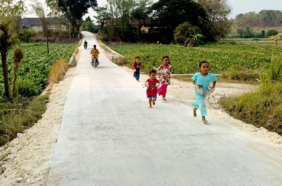 Anggi bersama teman-temannya bermain dan berlari di jalan cor hasil pembangunan TMMD ke-129 Kodim 0813 Bojonegoro di Dusun Mundu, Desa Kesongo, Kecamatan Kedungadem, Kabupaten Bojonegoro, Minggu (09/08/2026). Foto: Deni Ari Pandi/Sumber: TMMD Bojonegoro.