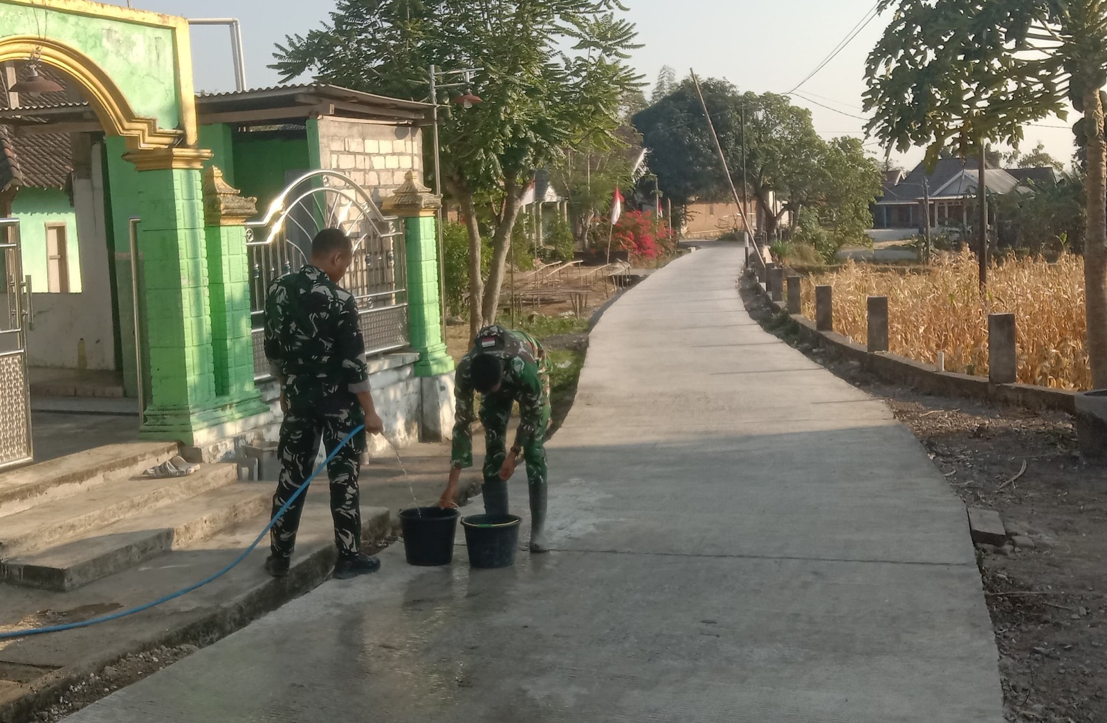 Personel Satgas TNI Manunggal Membangun Desa (TMMD) ke-129 Kodim 0813/Bojonegoro bersama warga melaksanakan perawatan jalan beton yang telah selesai dicor di Dusun Kedungpandan, Desa Kesongo, Kecamatan Kedungadem, Kabupaten Bojonegoro, Minggu (2/8/2026).