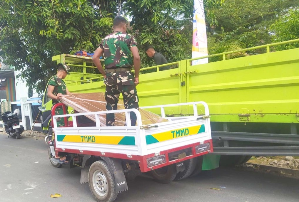 Di Desa Kesongo, Kecamatan Kedungadem, Kabupaten Bojonegoro, Sabtu (1/8/2026), personel Satgas TMMD memanfaatkan kendaraan roda tiga untuk mengangkut material bangunan menuju rumah-rumah penerima manfaat yang berada di gang sempit.