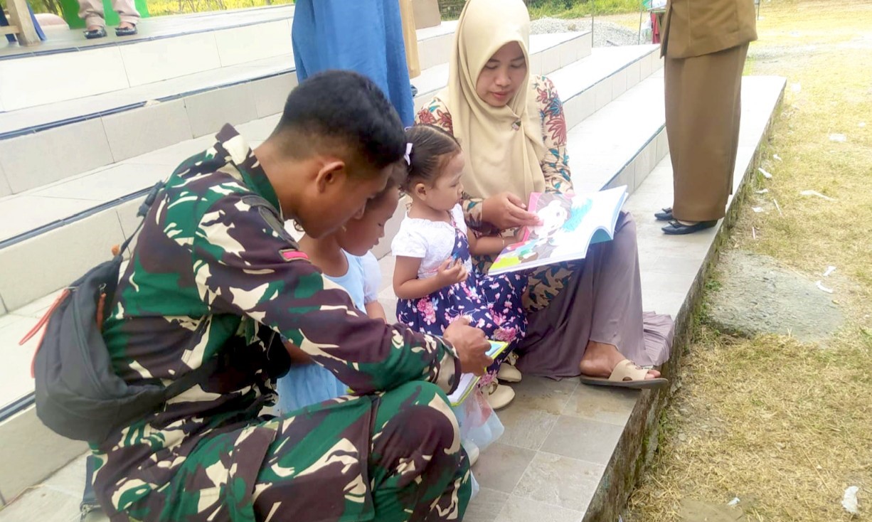 Prada Adnan FZ, anggota Satgas TMMD ke-129 Kodim 0813/Bojonegoro, mendampingi anak-anak membaca buku dalam kegiatan Layanan Terpadu Perpustakaan Desa (LTPD) di Pendopo Balai Desa Kesongo, Kecamatan Kedungadem, Selasa (4/8/2026). Foto : Deni Aripandi/Sumber TMMD Bojonegoro