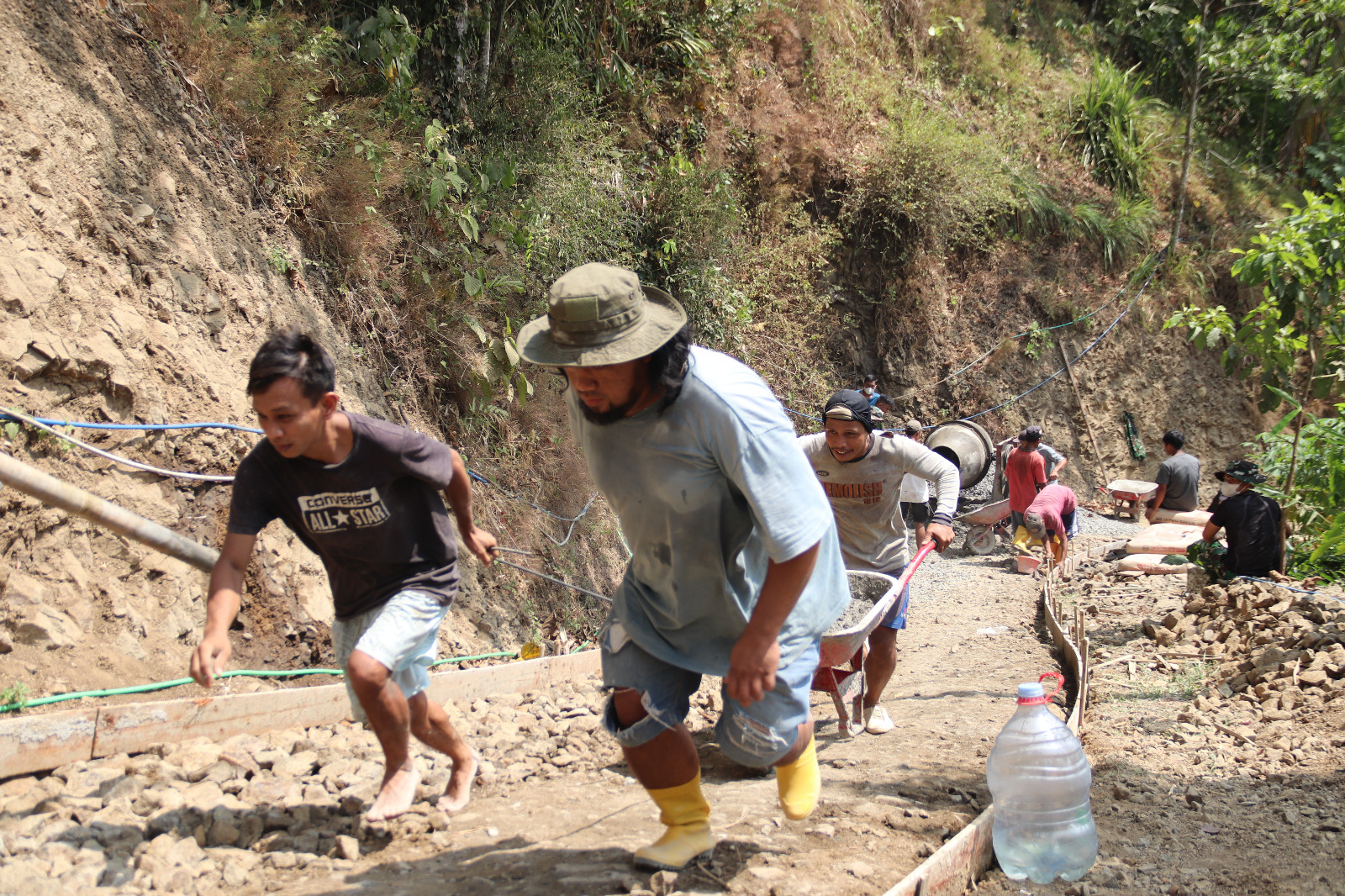 Gotong Royong di Tanjakan: Dua warga Desa Gumelem Kulon bekerja sama menarik dan mendorong angkong berisi adukan beton menuju lokasi pengecoran rabat beton dalam pelaksanaan TMMD Reguler ke-129 Kodim 0704/Banjarnegara, Jumat (7/8/2026).