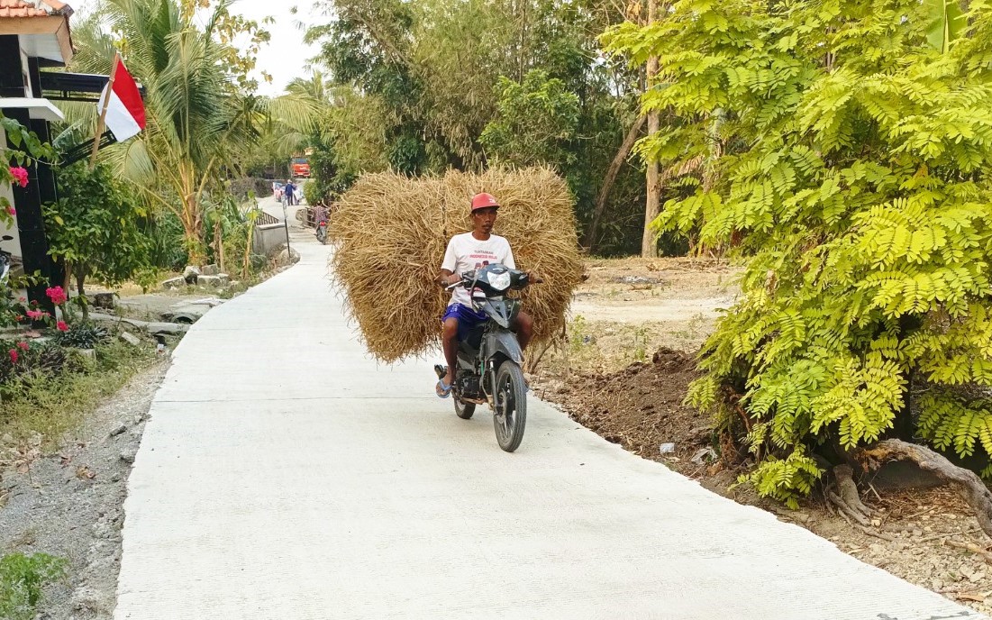 Warga Dusun Mundu melintas di jalan cor beton sepanjang 490 meter yang dibangun melalui program TMMD ke-129 Kodim 0813 Bojonegoro di Desa Kesongo, Kecamatan Kedungadem, Kabupaten Bojonegoro, Minggu (09/08/2026). Foto: Deni Aripandi/Sumber TMMD Bojonegoro.