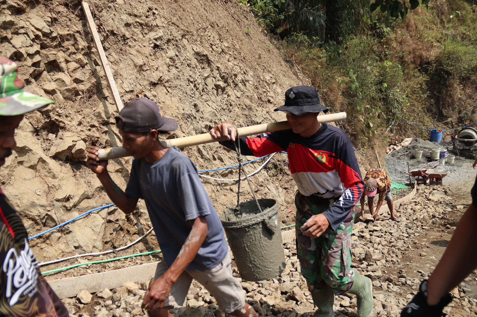 Foto: Praka Ari bersama Tono, warga Desa Gumelem Kulon, memikul adukan beton menggunakan bambu menuju lokasi pengecoran rabat beton pada pelaksanaan TMMD Reguler ke-129 Kodim 0704/Banjarnegara di Dusun Kunir RT 01/09, Kecamatan Susukan, Kamis (6/8/2026). Kebersamaan TNI dan warga menjadi kekuatan utama dalam mempercepat pembangunan infrastruktur desa. Foto: Deni Aripandi/Pendim Banjarnegara.