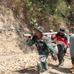 Totalitas Satgas TMMD: Pelda Ratam bersama rekannya memikul ember berisi adukan beton menuju lokasi pengecoran rabat beton di Dusun Kunir RT 01/09, Desa Gumelem Kulon, Kecamatan Susukan, Jumat (7/8/2026). Cara tersebut dilakukan untuk memperlancar distribusi material di medan yang sempit dan menanjak.
