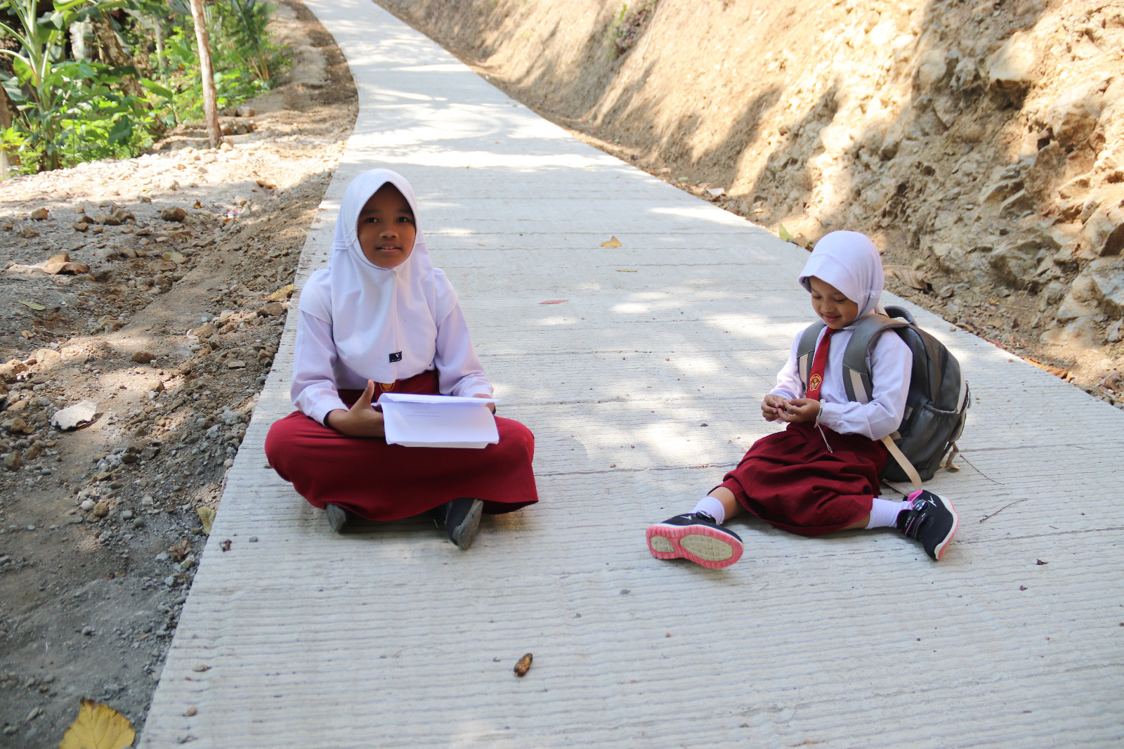 Yubna dan Quin, siswa SDN 6 Gumelem Kulon, menikmati jalan rabat beton hasil program TMMD Reguler ke-129 di Dusun Kunir RT 01/09, Desa Gumelem Kulon, Kecamatan Susukan, Kabupaten Banjarnegara, Rabu (12/8/2026). Foto: Deni Flamboyan/Sumber: Tim TMMD Banjarnegara.