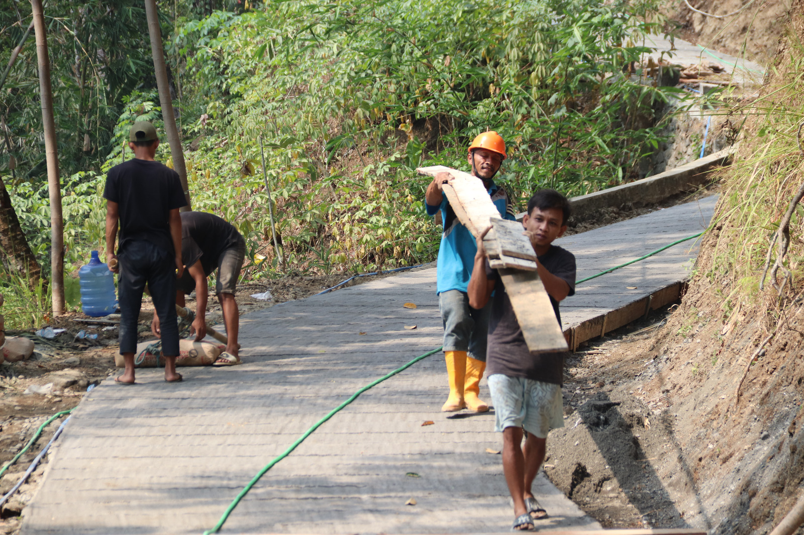Warga Desa Gumelem Kulon bersama anggota Satgas TMMD bergotong royong mengangkut semen dan material bekisting untuk mendukung pembangunan rabat beton sepanjang 737 meter, Sabtu (08/08/2026).