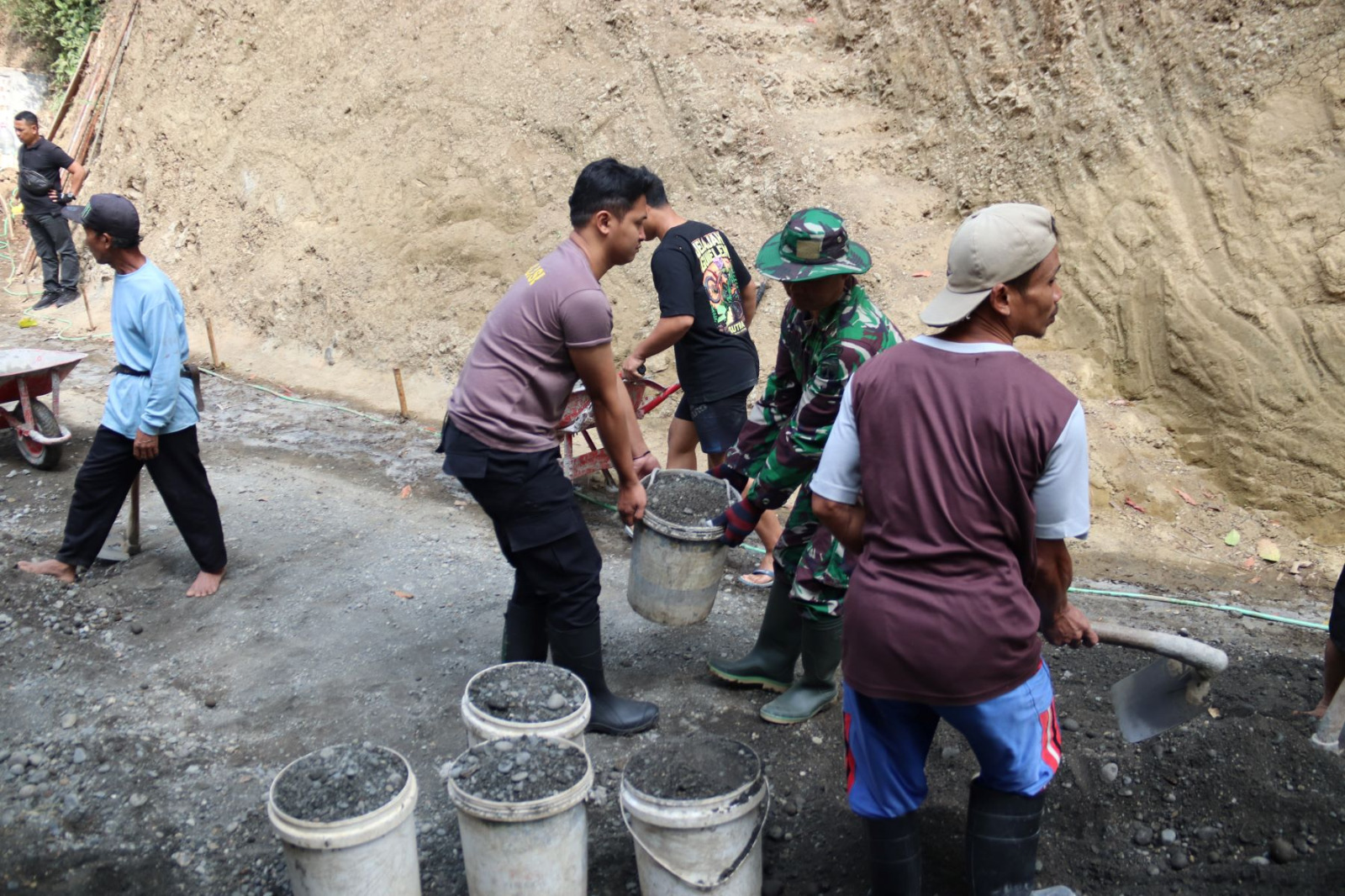 Personel TNI dan Polri bahu-membahu bersama warga melangsir batu split untuk mendukung pembangunan rabat beton di Dusun Kunir RT 01/RW 09, Desa Gumelem Kulon, Kecamatan Susukan, Minggu (2/8/2026).