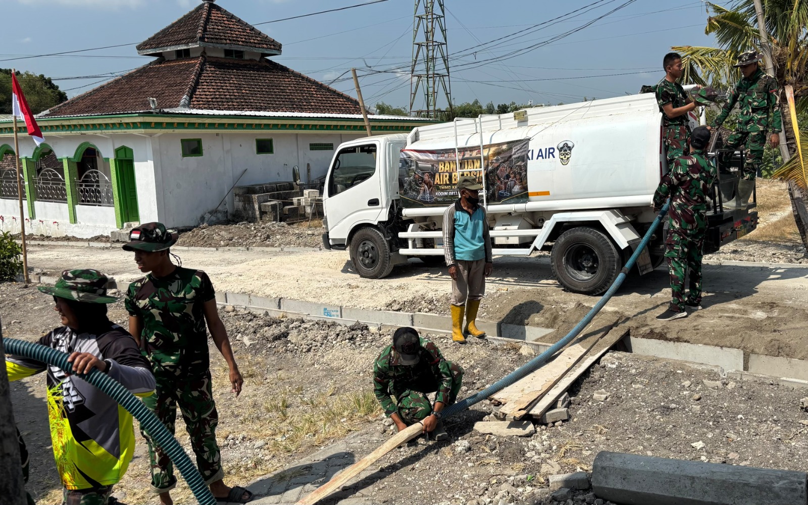Bergandengan tangan dengan Babinsa Desa Kesongo, Serka Lasmidi, para personel Satgas TMMD menerjang terik musim kemarau untuk mendistribusikan air bersih langsung ke rumah-rumah warga di Dusun Krebet RT.013 RW.006, Desa Kesongo, Kecamatan Kedungadem, Kabupaten Bojonegoro, Selasa (4/8/2026).