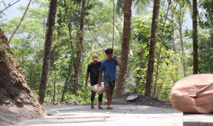 Dengan memikul dua sak semen menggunakan bambu di atas pundak, keduanya hilir mudik mengantarkan material menuju titik pengecoran rabat beton sepanjang 737 meter, lebar 2,5 meter, dan tebal 0,15 meter di Dusun Kunir RT 01/09, Desa Gumelem Kulon, Kecamatan Susukan, Rabu (5/8/2026).