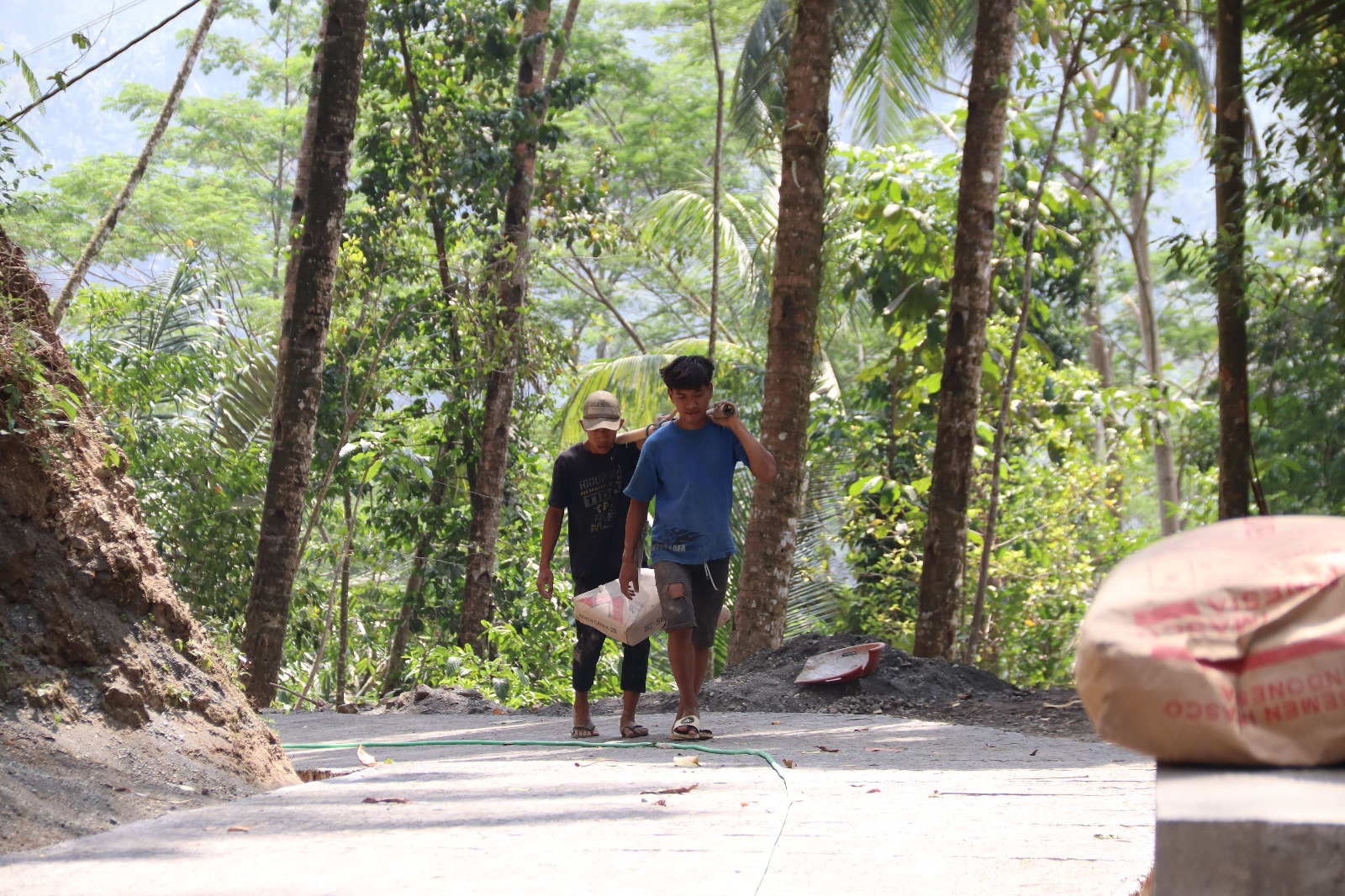 Dengan memikul dua sak semen menggunakan bambu di atas pundak, keduanya hilir mudik mengantarkan material menuju titik pengecoran rabat beton sepanjang 737 meter, lebar 2,5 meter, dan tebal 0,15 meter di Dusun Kunir RT 01/09, Desa Gumelem Kulon, Kecamatan Susukan, Rabu (5/8/2026).