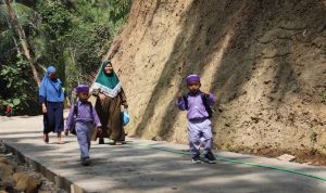 Noval, anak PAUD Desa Gumelem Kulon, melintas di lokasi pembangunan rabat beton TMMD Reguler ke-129 Kodim 0704/Banjarnegara sambil menyapa anggota Satgas yang sedang bekerja di Dusun Kunir RT 01/09, Kecamatan Susukan, Kamis (6/8/2026). Pembangunan jalan TMMD menjadi harapan baru bagi generasi muda desa. Foto: Deni Aripandi/Sumber TMMD Banjarnegara