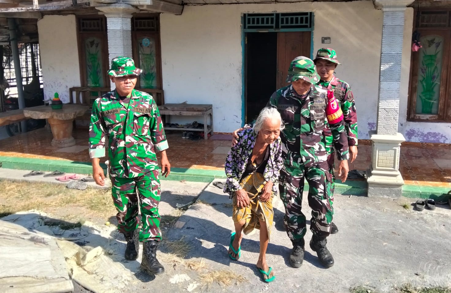 Babinsa Desa Kesongo Serka Lasmidi mendampingi Mbah Kasidah melihat proses rehabilitasi rumah putranya, Bapak Ladi, dalam program TMMD ke-129 Kodim 0813 Bojonegoro di Desa Kesongo, Kecamatan Kedungadem, Jumat (7/8/2026).